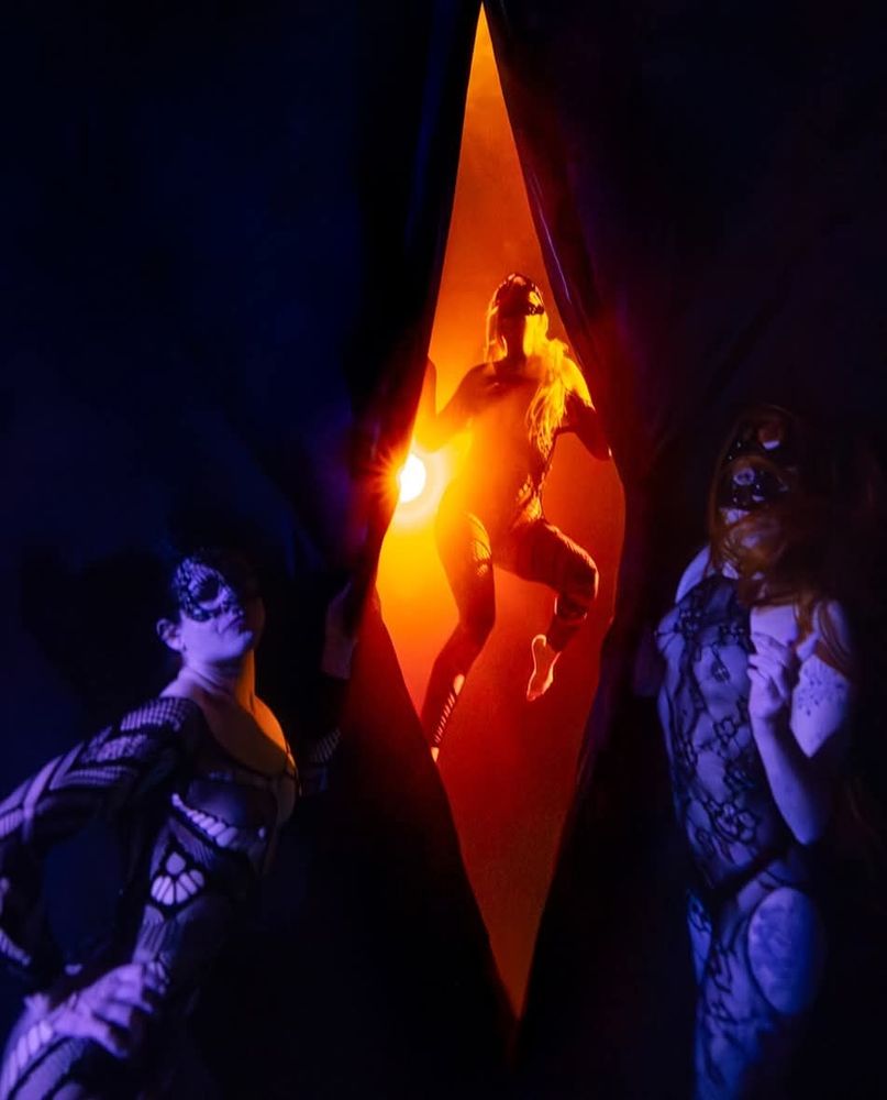 Three women underwater performing a peepshow. Two women are opening a curtain to reveal the third woman. 