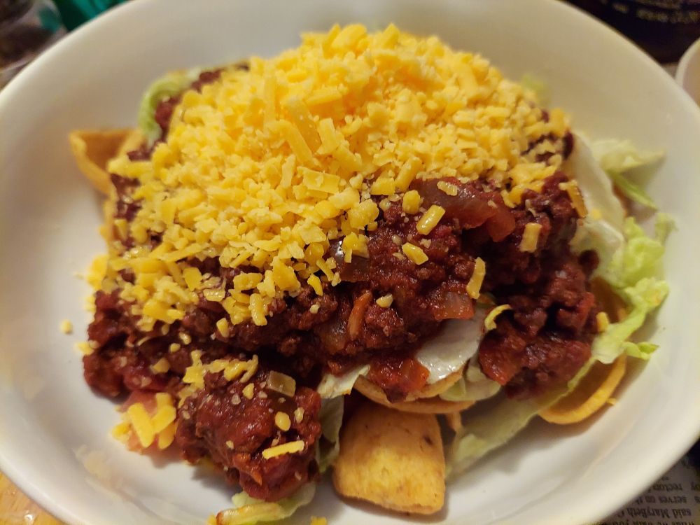 This is a dish that my dad used to make often. It's made with his homemade chili served on top of Fritos, lettuce, tomato, onions and then topped with grated or shredded cheddar cheese. This photo shows the dish before mixing it all together.