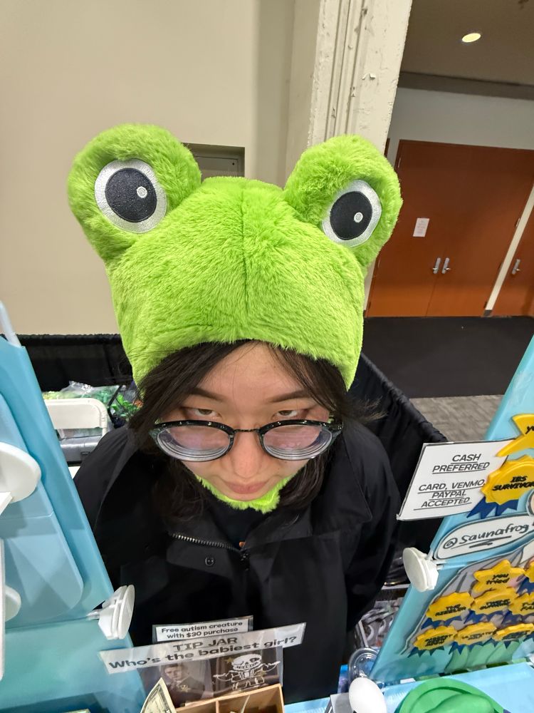 0.5 camera angle of saunafrog staring deep into your soul while wearing a frog hat