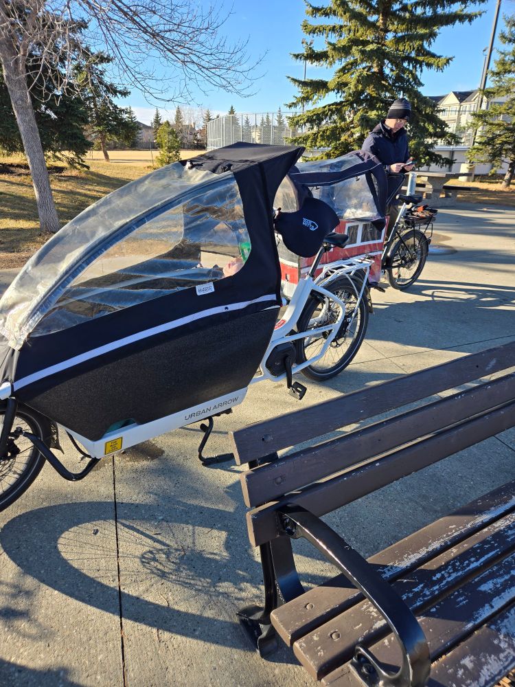 A toddler peaks out under the cover of a cargo bike, but fast asleep.