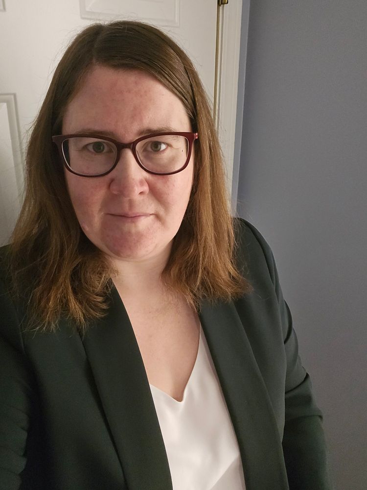 Picture of a woman with shoulder length brown hair wearing a green blazer and white blouse 