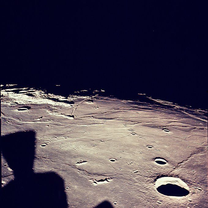 "This west-looking image of the landing site in the southwestern Sea of Tranquility (Mare Tranquilitatis) was taken from the lunar module one orbit before descent, while still docked to the command module. The Tranquility base site is near the shadow line, just to the right of center.
The large crater at the lower right is the 23 km diameter Maskelyne, centered at 2.2 N, 30.1 E. The large black object in the lower left is not a shadow but a LM thruster in the camera field of view. (Apollo 11, AS11-37-5437)"