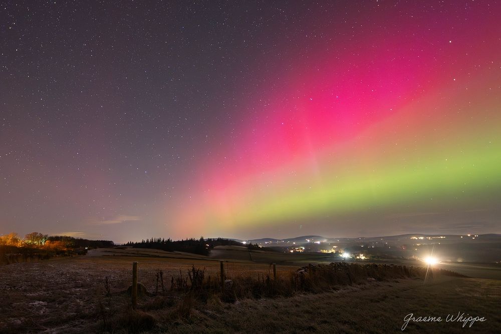 Oh man, this photo Graeme Whipps took on December 1, 2023, in Chapel of Garioch, Scotland, just blows you away. It's that rare moment when a delicate green aurora down low mixes with a quiet, steady red SAR arc up high. Softly snowy fields lie dark and hushed in the foreground, dotted with a few farm buildings and faint lights far off on the horizon. The sky starts with soft green glows near the ground, fades into deep pinks higher up, and then there's this broad, calm red band stretching peacefully overhead. A scatter of stars peeks through, and the whole thing feels almost unreal—like the universe quietly showing off its magic.