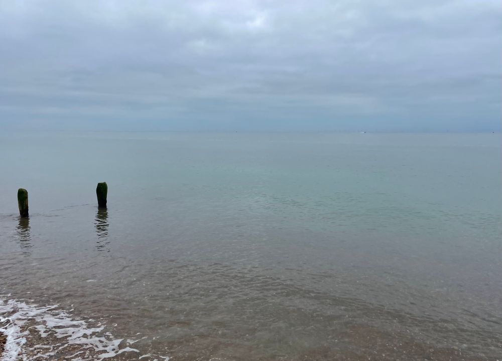 Calm sea merging into the sky with two wooden groynes visible