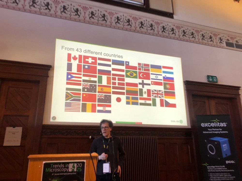A photo of Matthew Hartley of the BioImage Archive standing at a podium in front of a slide showing the flags of 43 different countries which are making use of the image archive.