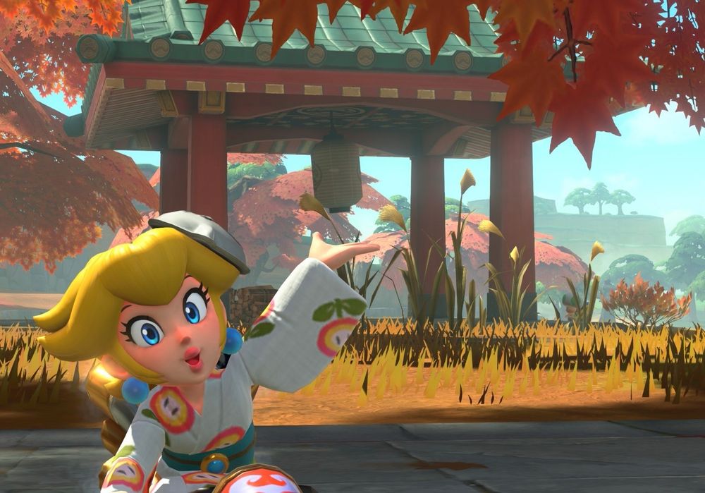 screenshot of Princess Peach in her yukata outfit at Cheep Cheep Falls, posing with her hand out in front of a small pagoda-like structure with a lantern hanging from its ceiling 
orange maple leaves frame the image at the top, and more trees can be seen from the left side behind Peach