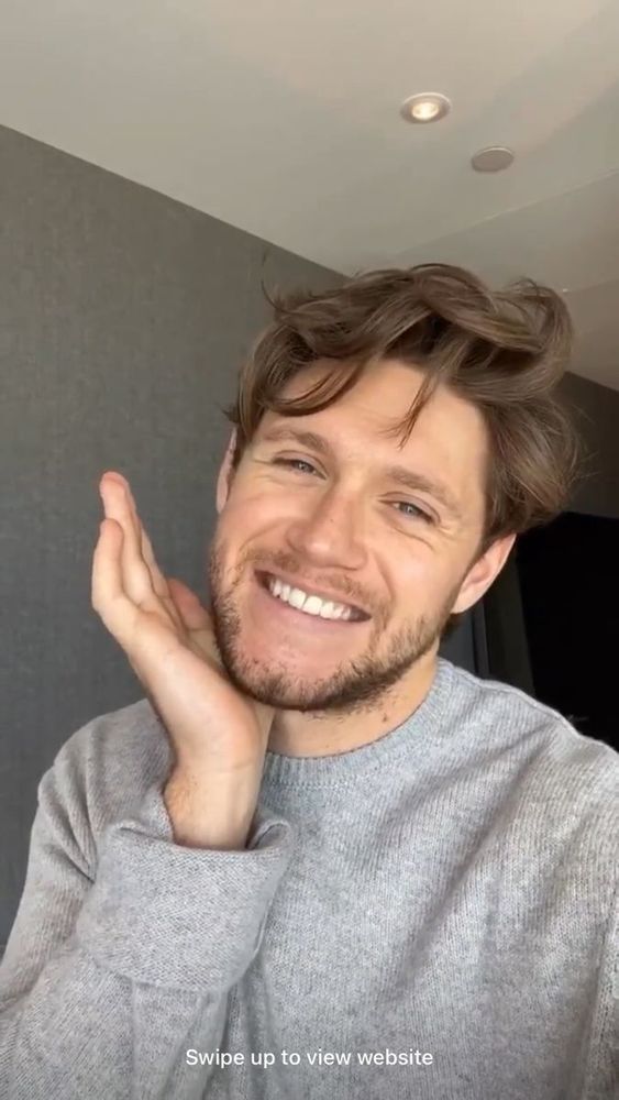 Niall Horan smiling with a hand under his chin