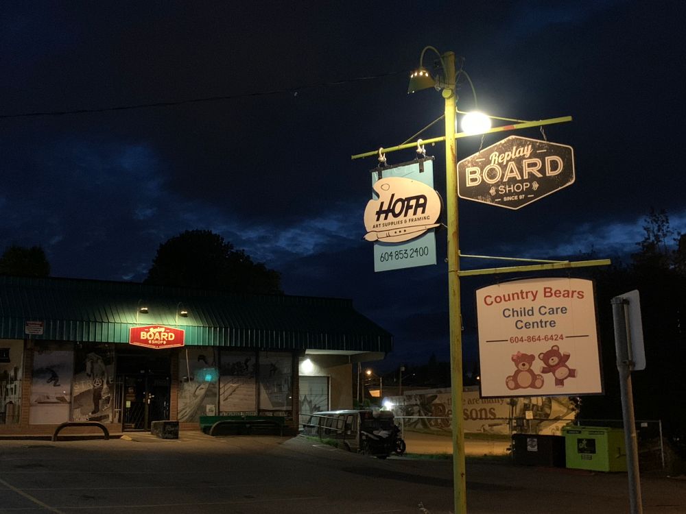 Three signs under a lamp read replay board shop, Hofa art suppplies and framing, country bears childcare centre.