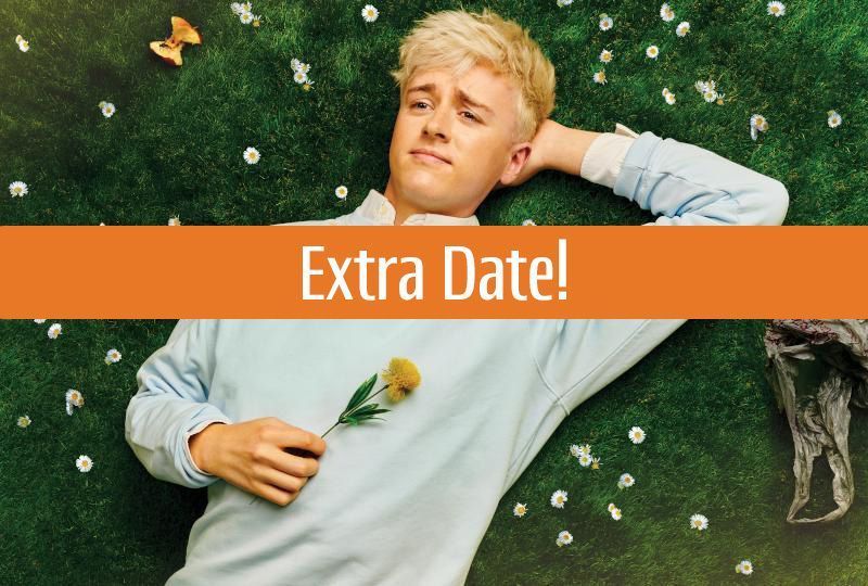 Photo of Daniel Foxx lying on some grass with daisies, an apple core and a plastic bag surrounding him, holding a yellow flower to his chest. An orange banner with the text 'Extra Date!' in white is overlaid across the middle of the image.