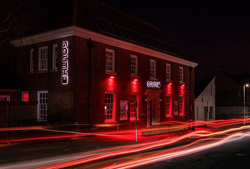 Photo of the front of the South Street building at night, lit up with red lighting. Photo by Steve Foster Images.
