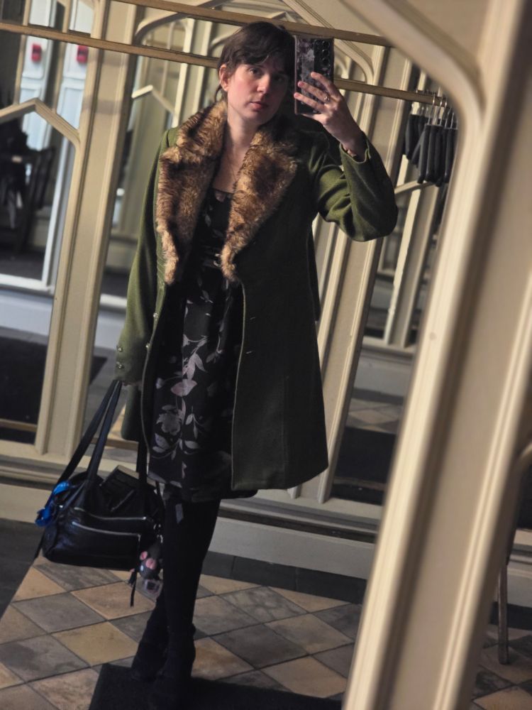 Jax in her local mirror in a green broadcloth coat with a faux fur collar