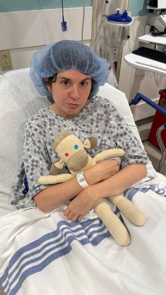 Jax in a surgical gown and cap with her sock monkey