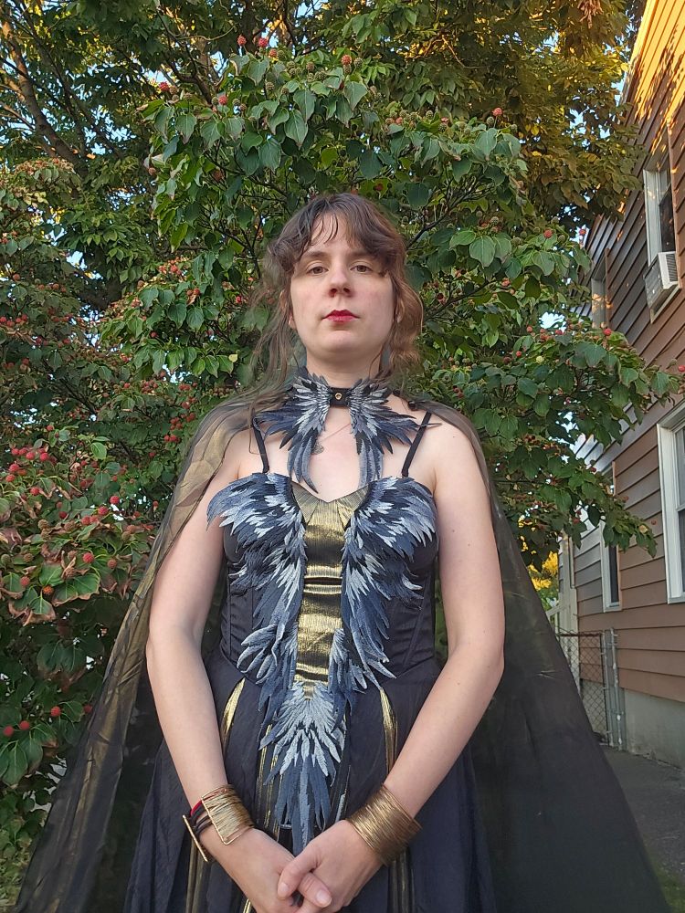 Jax stands in front of her dogwood tree wearing a black and gold dress and gold cape