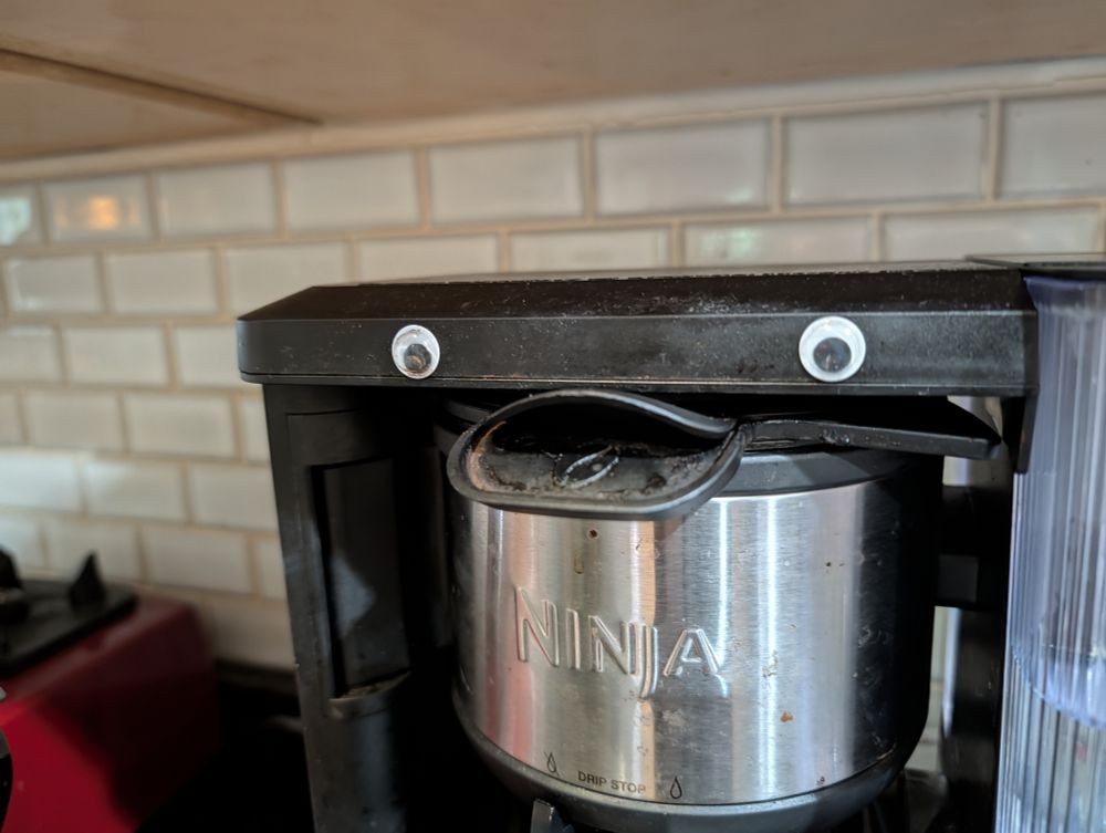 A coffee maker with googly eyes on it and part of it sticks out like a little beak