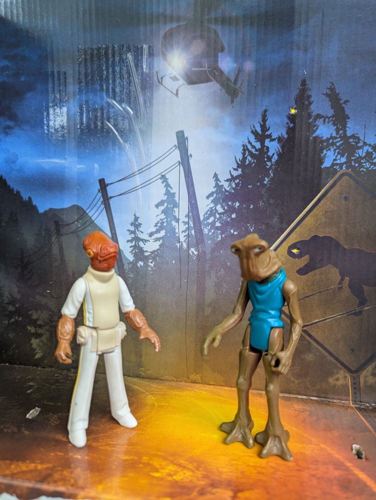 Admiral Ackbar and his friend Hammerhead find themselves suddenly in Jurassic Park under a helicopter's spotlight! Action figures, inside the packaging for the Jurassic World Uno Attack game in which you get a little plastic dinosaur head that you load cards into and instead of drawing a card from a pile when you can't put a card down you tap down on the dinosaur's nose and there's a random chance it will spit a random number of cards at you! But at most like, 6