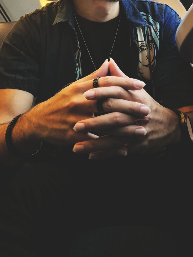 Hands with fingers locked, pointy nails, veins, outfit black and blue just like the ring and bracelet