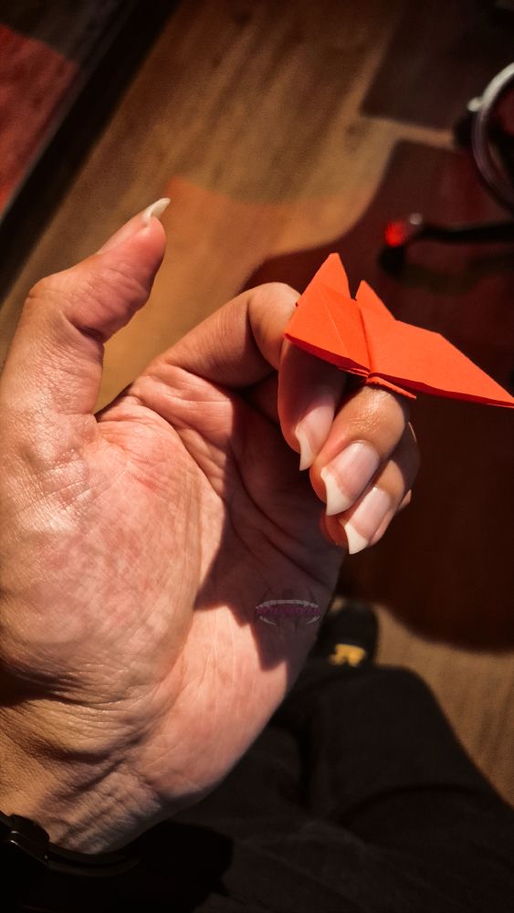 Handpic pointy nails holding red origami butterfly between the fingers.