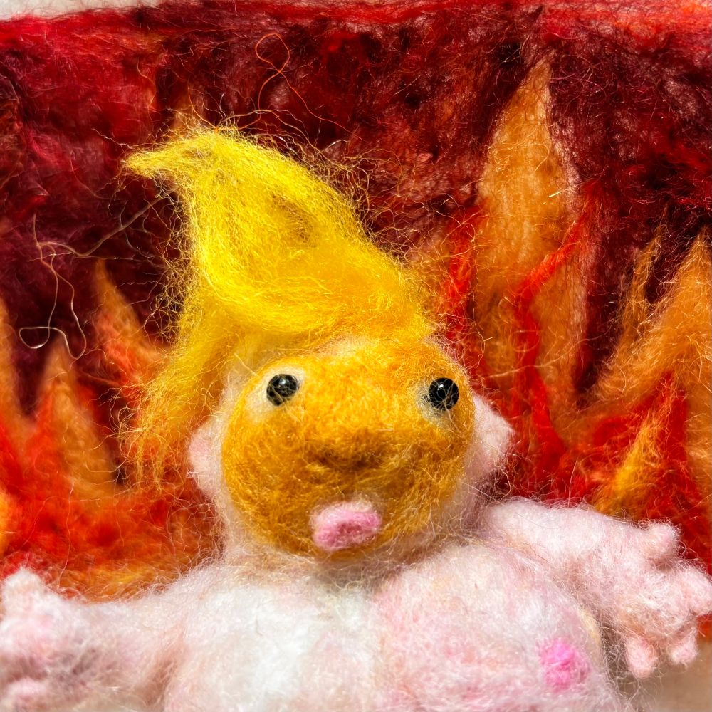 Fat baby trump made of wool looking confused in front of a fiery hellscape full of flames. He’s creepy unhinged and fucking ugly as sin. crafting a rebellion fiber arts