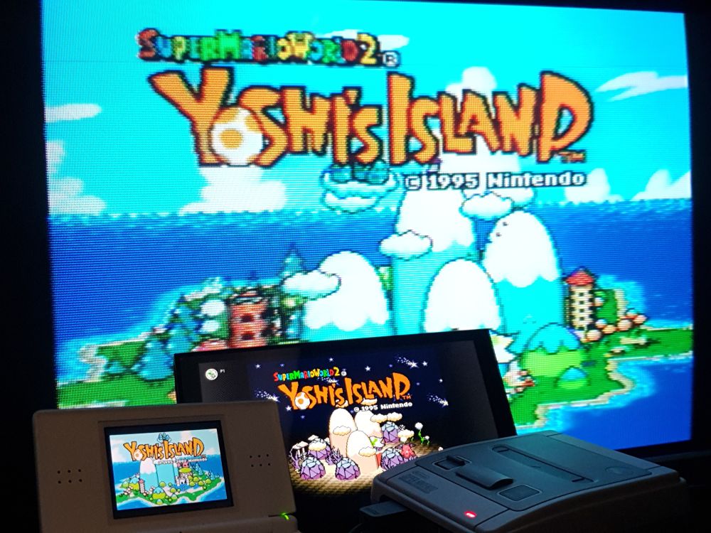 The title screen for Super Mario World 2: Yoshi's Island, displayed on three screens:
A CRT TV (a PAL SNES Classic Edition is plugged in, shown in front)
A Nintendo Switch 2 (showing a completed game)
A Nintendo DS lite (running the GBA version)