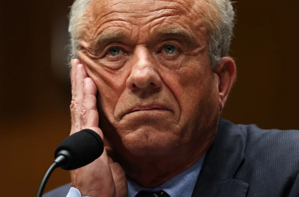 RFK Jr in a pensive pose at a microphone with a disturbing trump-esque 