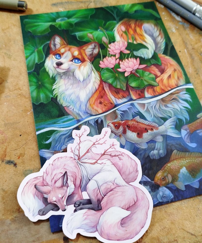 Photo of a print, a fox with koi and lotus plants and a sticker of a pink fox 