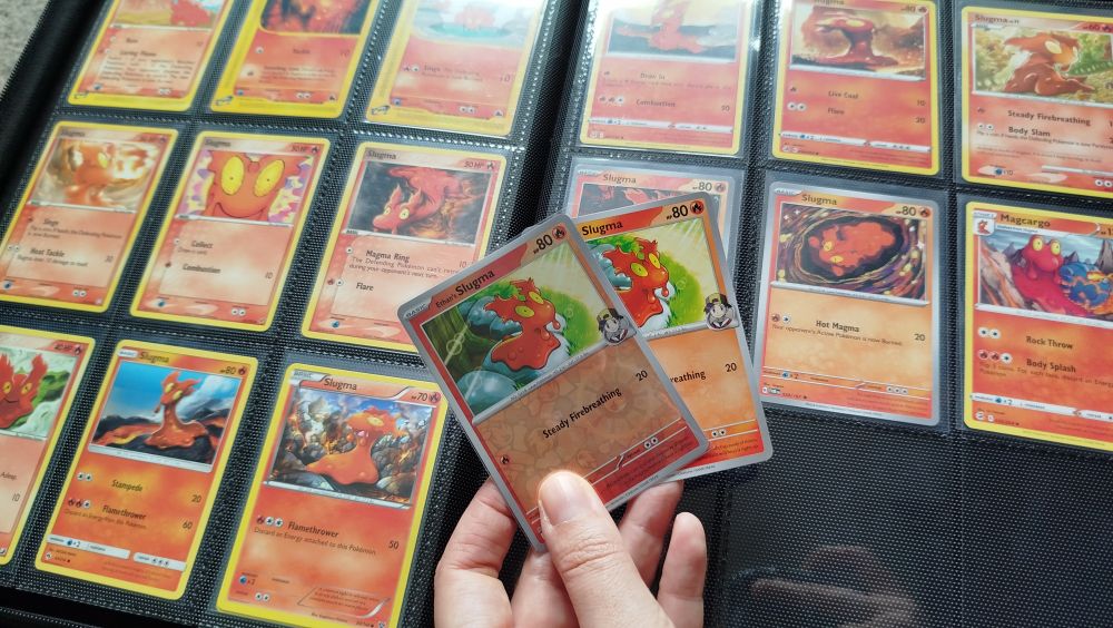 An open binder of Pokémon trading cards and two cards being held in a hand. The cards are all slugma.