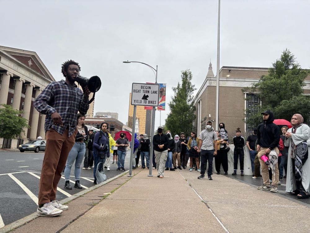 councilor Abdul Osmanu speaking into megaphone to crowd gathered on a sidewalk in Hartford