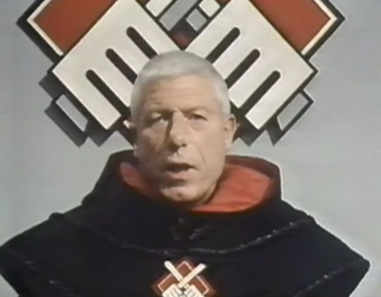 John Woodvine as Mordrin, Prior and ruler of the Knights of God, fascist black and red uniform and symbols