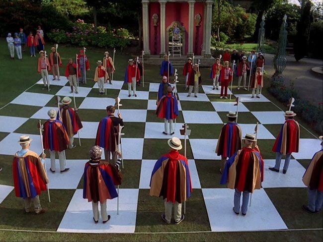 Village citizens in brightly-coloured capes stand in place on a life-sized chess board