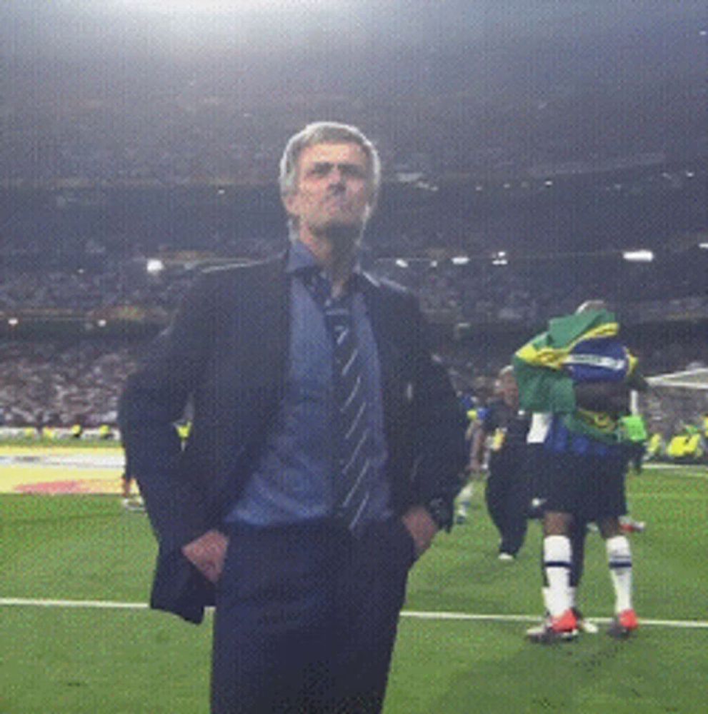 a man in a suit stands on a soccer field with his hands in his pockets