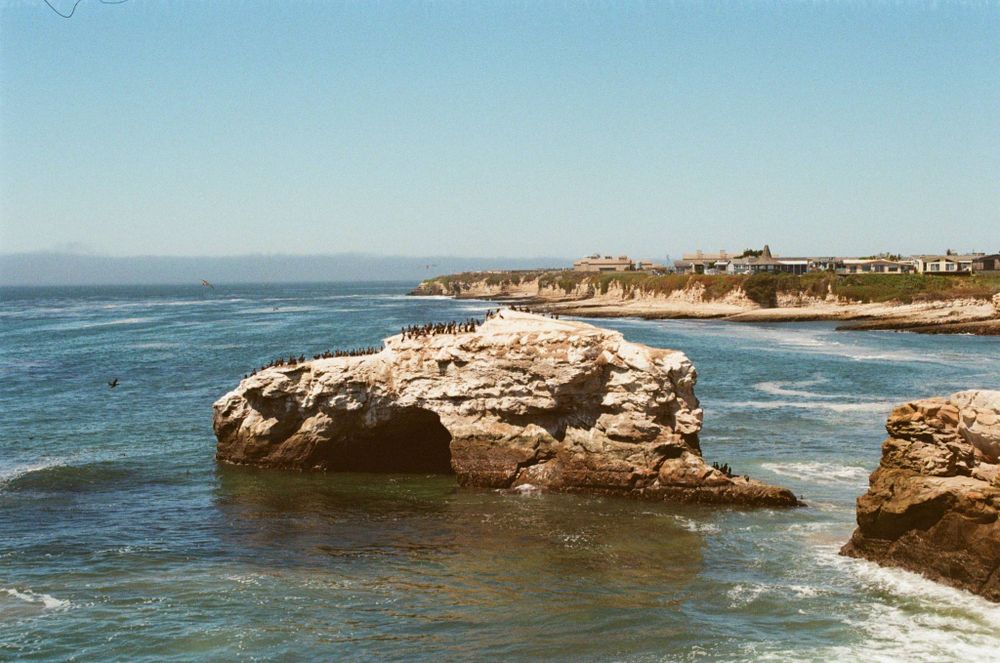 A closer view of the natural bridge - you can start to tell that there are birds on top of it. You can no longer see the breaking waves, and the buildings on the point in the background are more distinct. 50mm setting on the zoom lens.