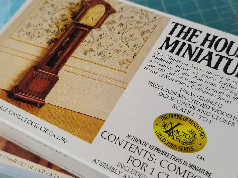 Close up of the box lid on another miniature furniture piece from the X-Acto House of Miniatures series, showing a preview image of a Willard tall case grandfather clock from the 1790s...