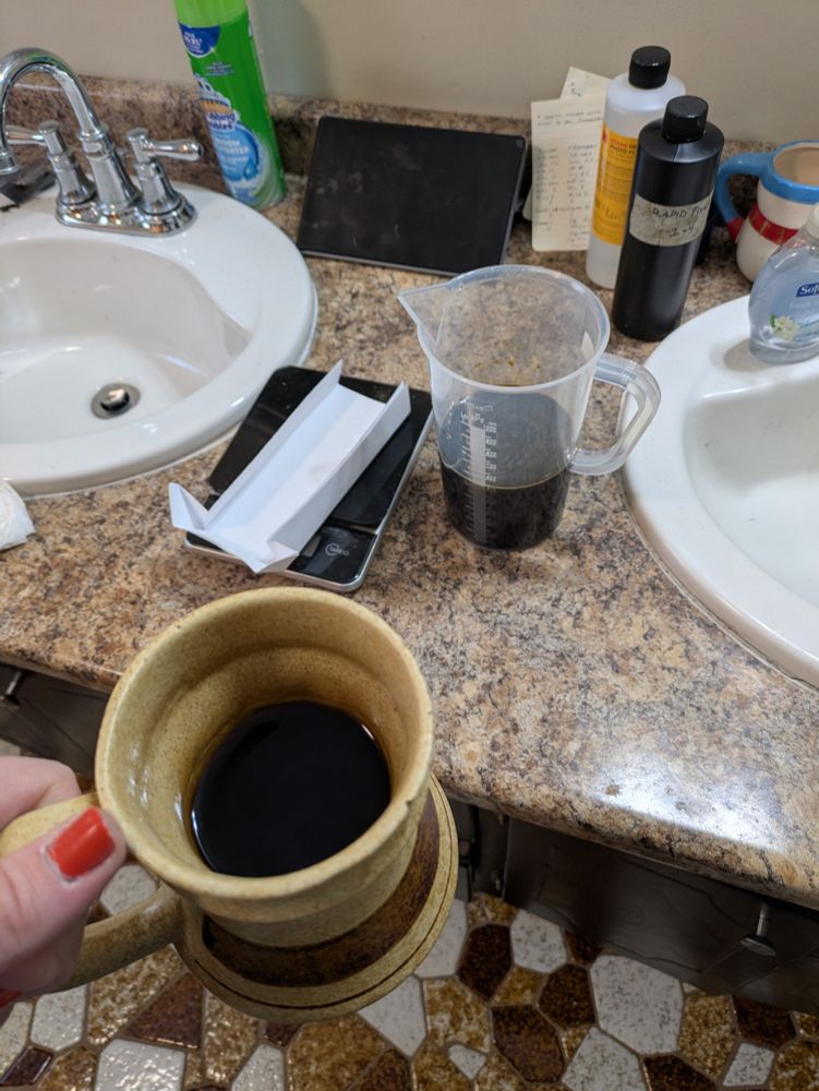 Mug of coffee and a pitcher of caffenol on a bathroom counter. 