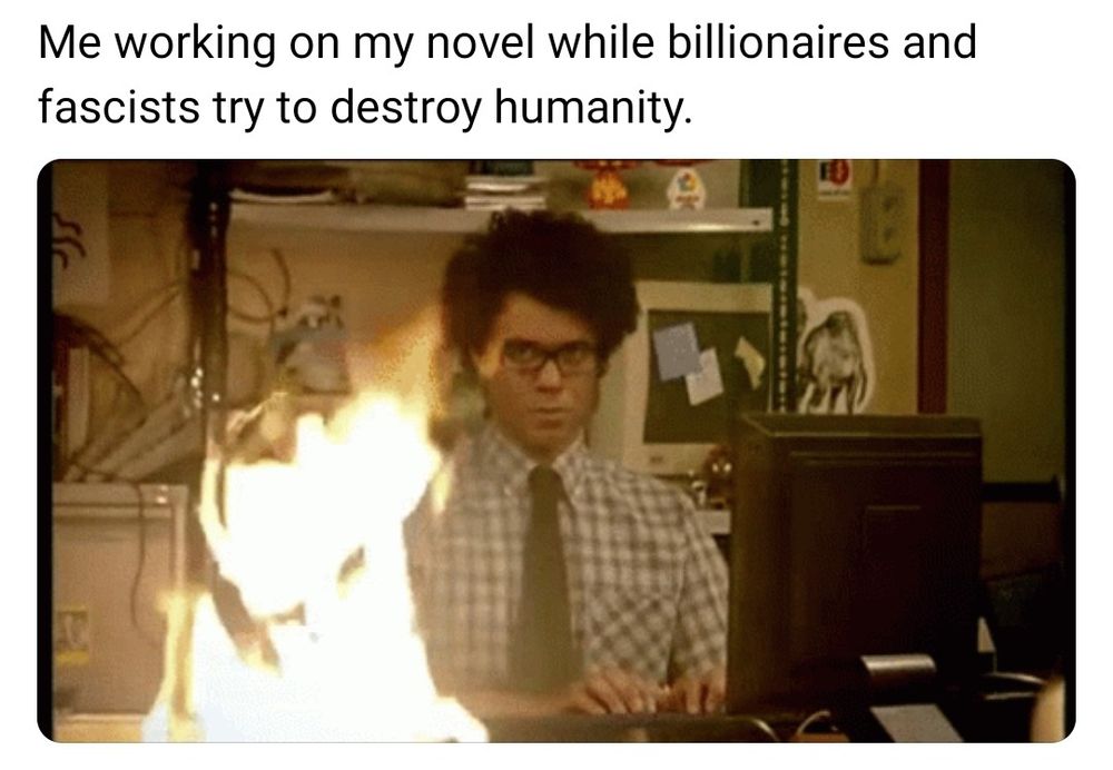 A man at a computer in a room on fire. Caption: me working on my novel about billionaires and fascists try to destroy humanity