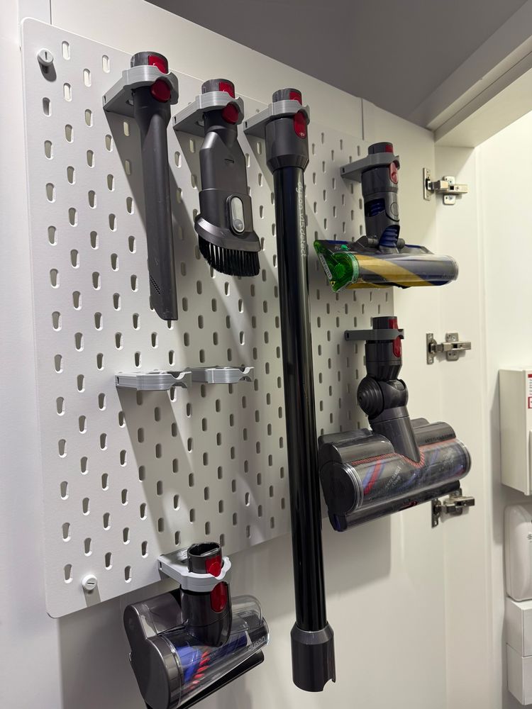 A picture showing Dyson vacuum accessories attached to an Ikea pegboard, they are attached using grey 3D printed brackets.