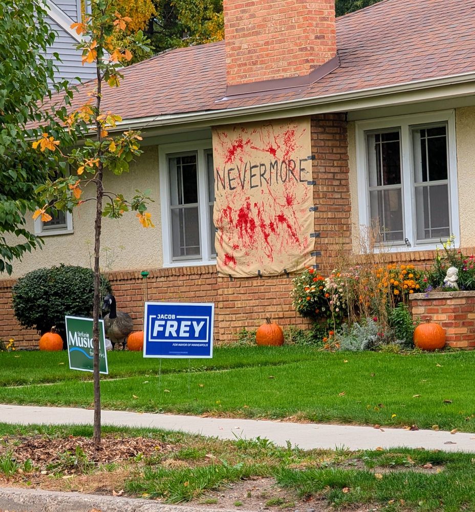 A Jacob Frey yard sign in front of a house with a large tan-colored tarp attached to the chimney with "NEVERMORE" scrawled on it over splattered red paint meant to look like blood