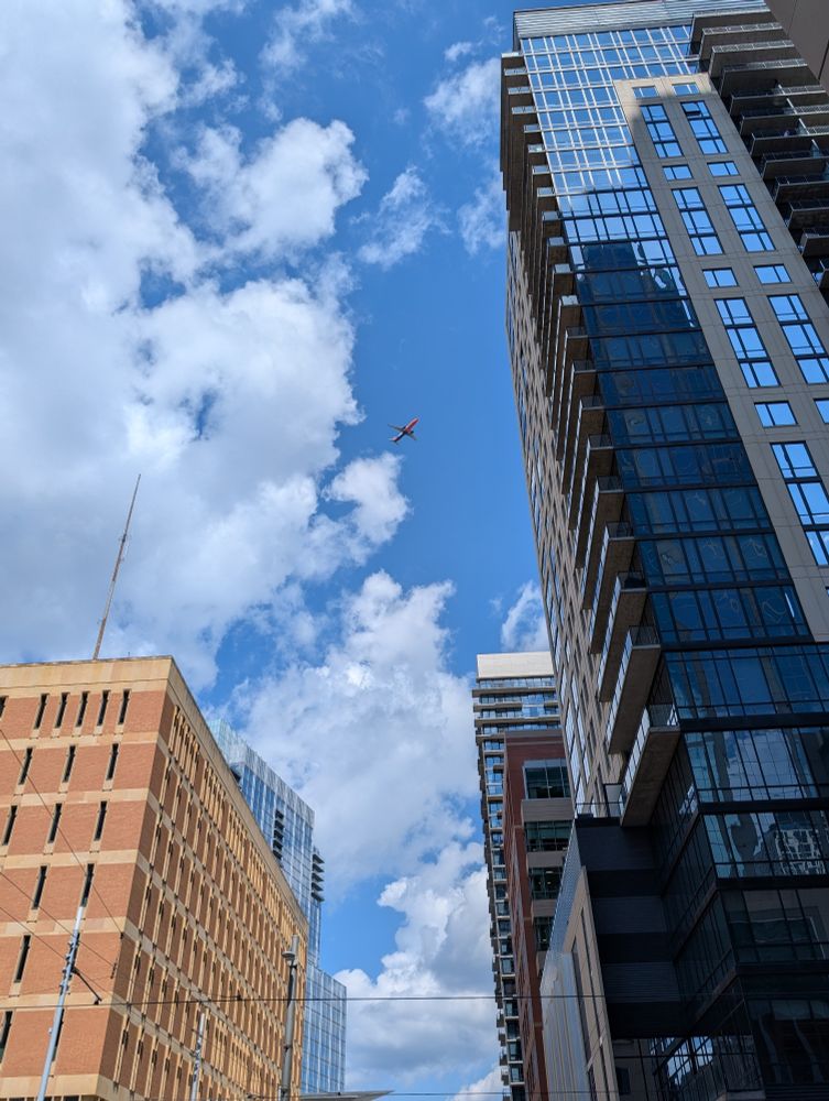 An orange, white, and blue Sun Country Airlines plane seen between buildings in downtown Minneapolis