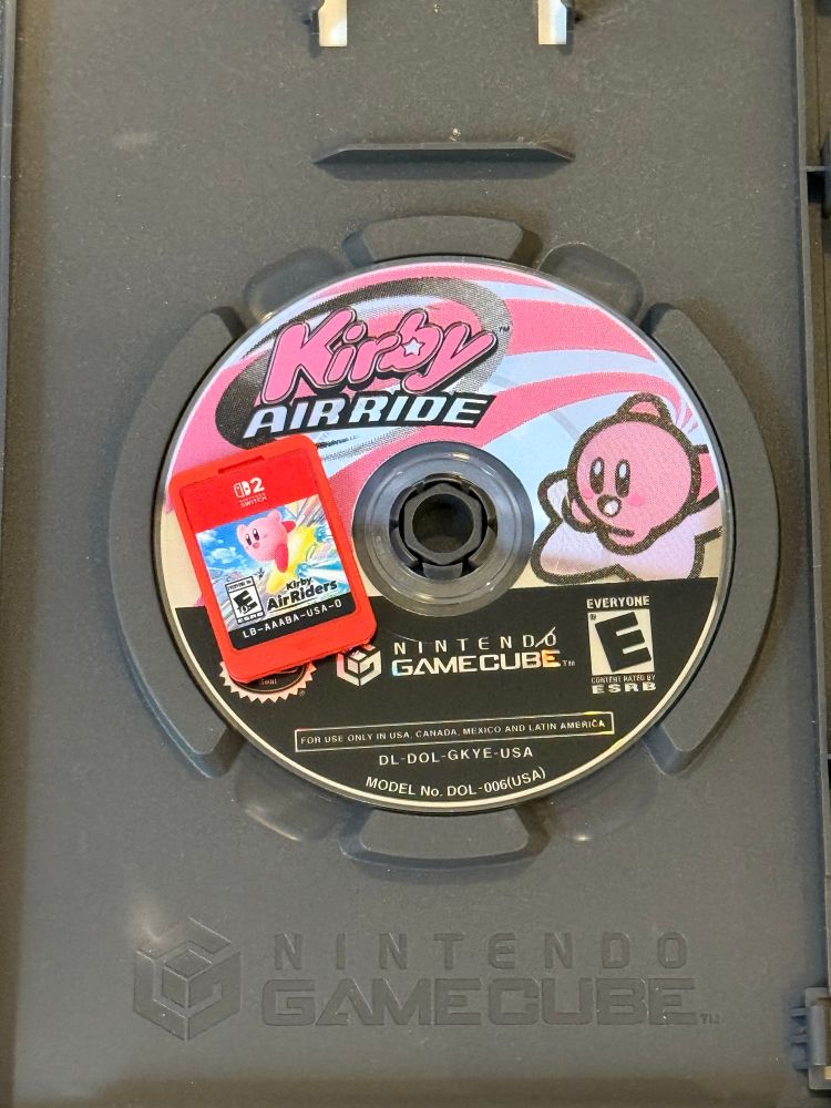 A photo of the red Kirby AirRiders Nintendo Switch 2 cartridge laying on top of the GameCube Kirby AirRide minidisc, still in its case. 