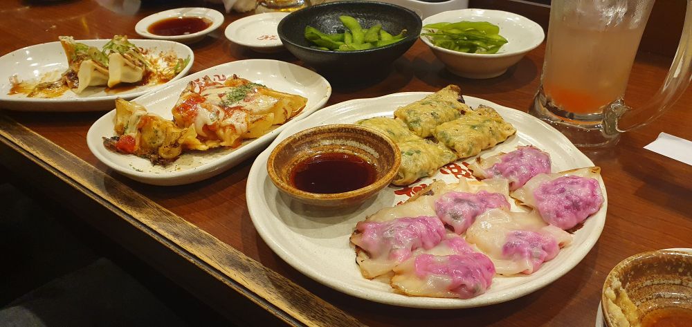 A picture of various Gyoza dishes with dipping sauces, edmame and drinks