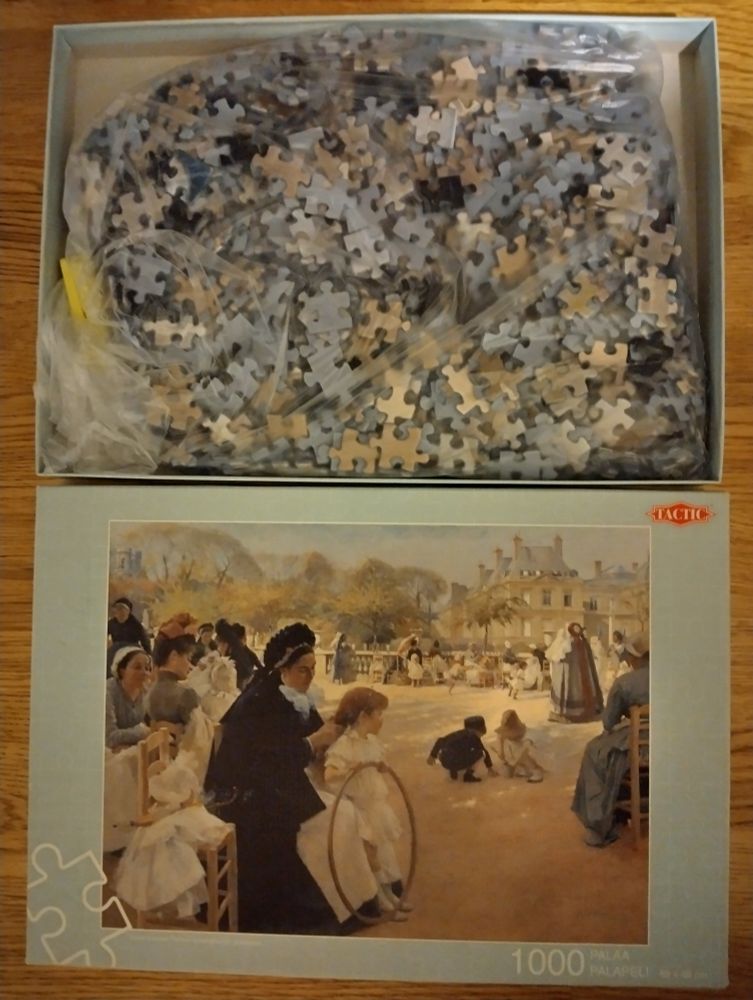 Palapeli laatikossaan. En osaa kuvailla kuvaa. Nainen letittää tytön hiuksia. Lapset leikkii hiekalla. Ihmiset istuu auringossa tuoleilla ilman pöytiä 