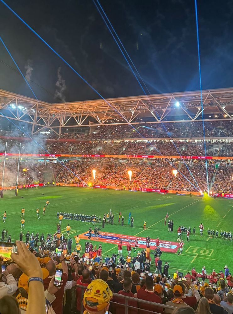 Photo shows the view of a playing field from the stands - players line up with a light show and crowd in the background. 