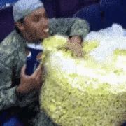 a man in a military uniform is eating a large bag of popcorn while holding a cup of pepsi .