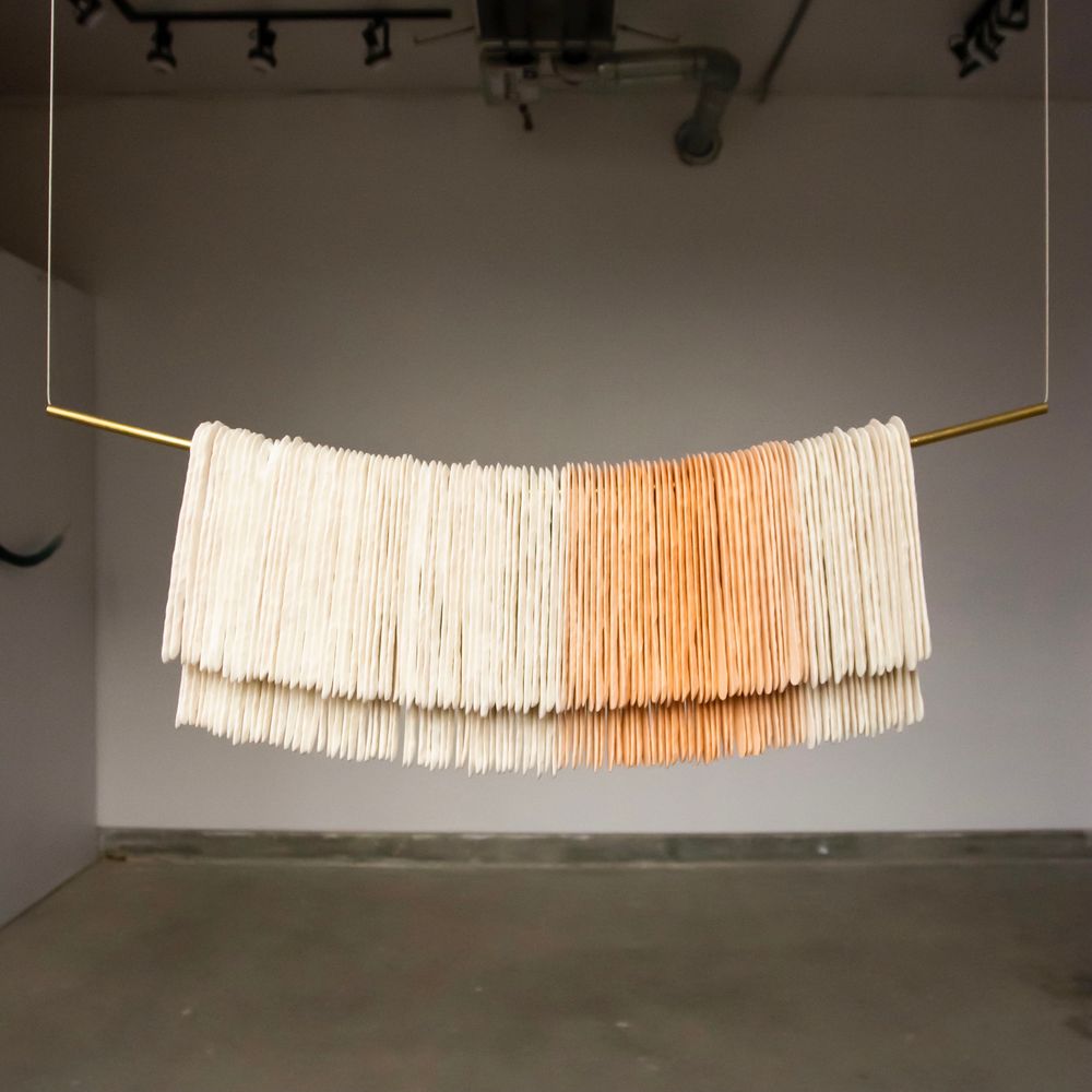 Many long flat translucent canes hang over a brass tube suspended by cable from the ceiling. 