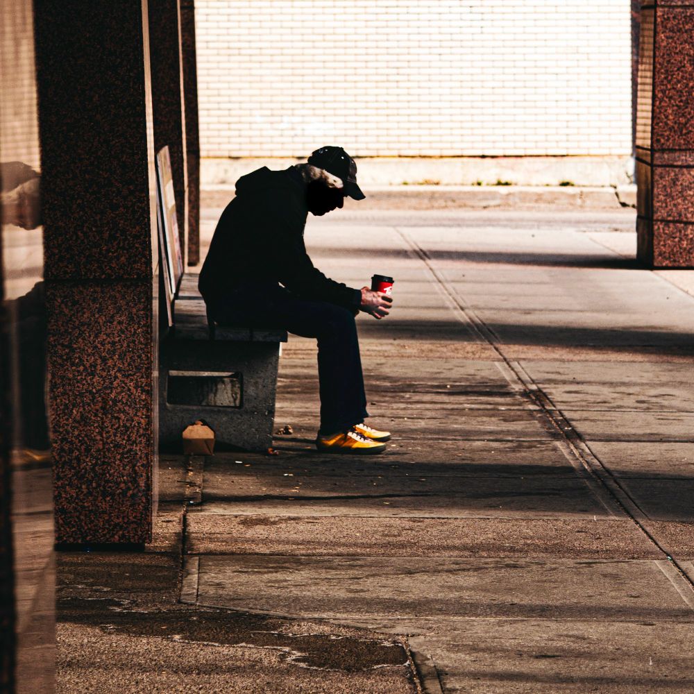 A sad man in bowling shoes sits on a bench. 
