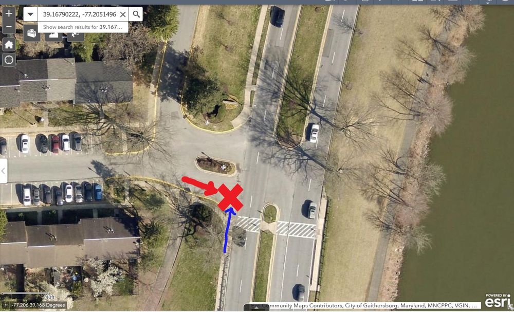 Satellite image of a divided entrance to an attached-house development with parking lot/streets. The driveway goes onto a three-lane divided road. One of the three legs of the intersection has a marked crosswalk (the south side). There is a red X in the driveway, indicating the location of the crash. There is a red arrow pointing east toward the red X, indicating the path of the driver getting ready to turn right (south). There is a blue arrow pointing north from the sidewalk into the unmarked crosswalk across the driveway, indicating the path of the teenager on the e-scooter.