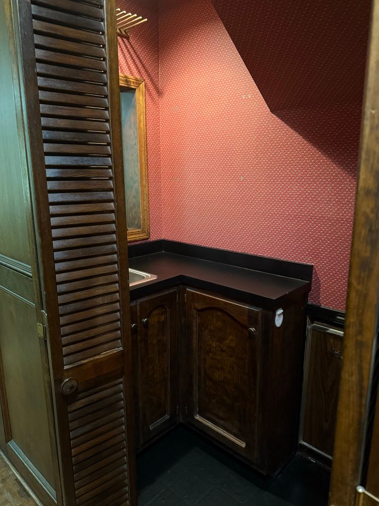 Before image showing the left half of the room with an L-shaped counter with cupboards below and a sink on the far left. The accordion doors are blocking most of the view of the sink.