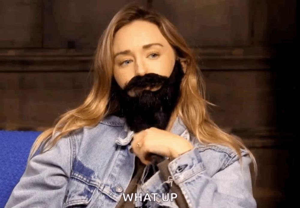 a woman with a fake beard and mustache says what up