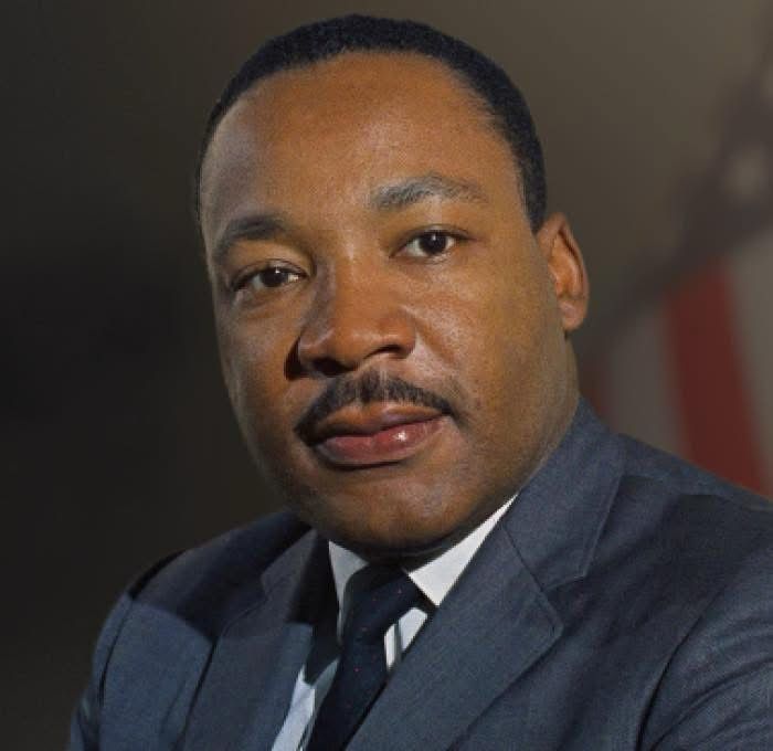 A color photo of Dr Martin Luther King Jr. He is wearing a dark blue suit and is slightly smiling 