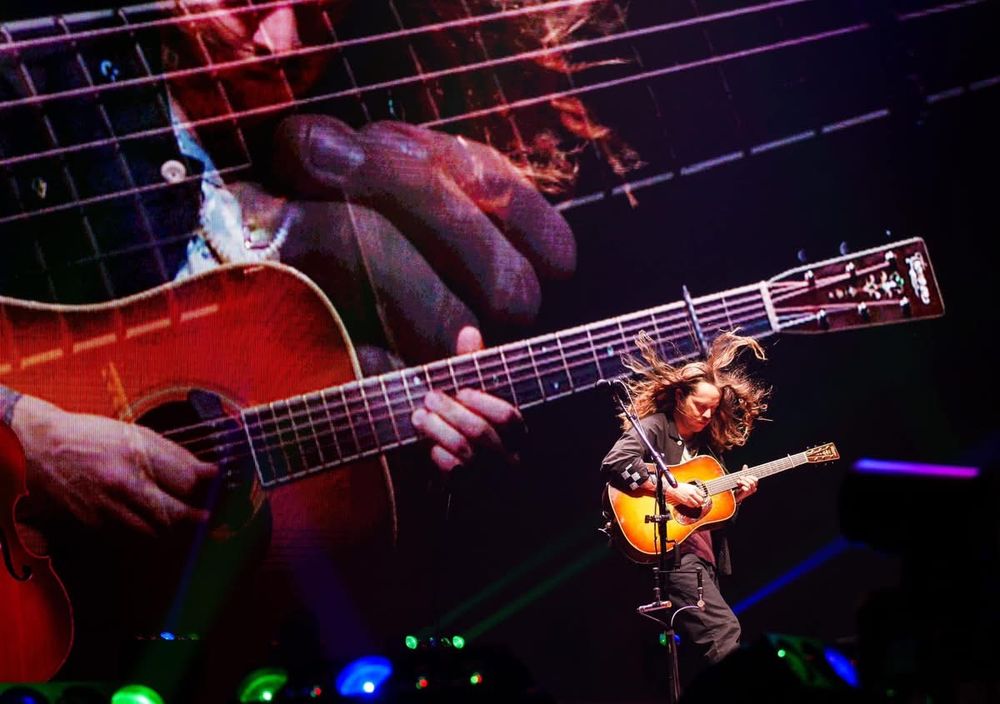 Billy Strings jamming out on stage while the screen behind shows a closeup of his playing guitar 