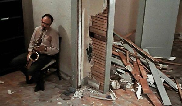 Man playing saxophone in a room that’s been partially destroyed 